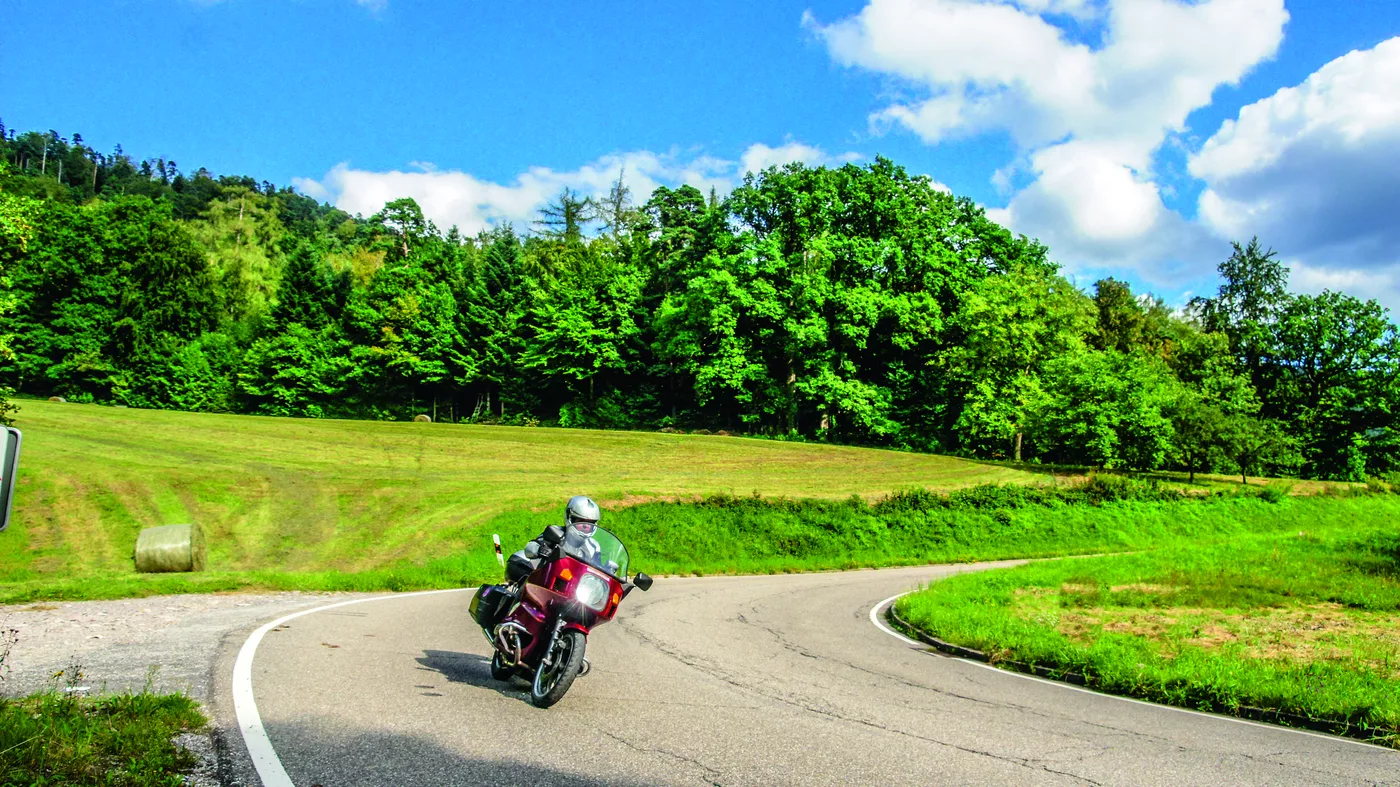 Motorrad auf einer Landstraße durch Wiesen und Wald